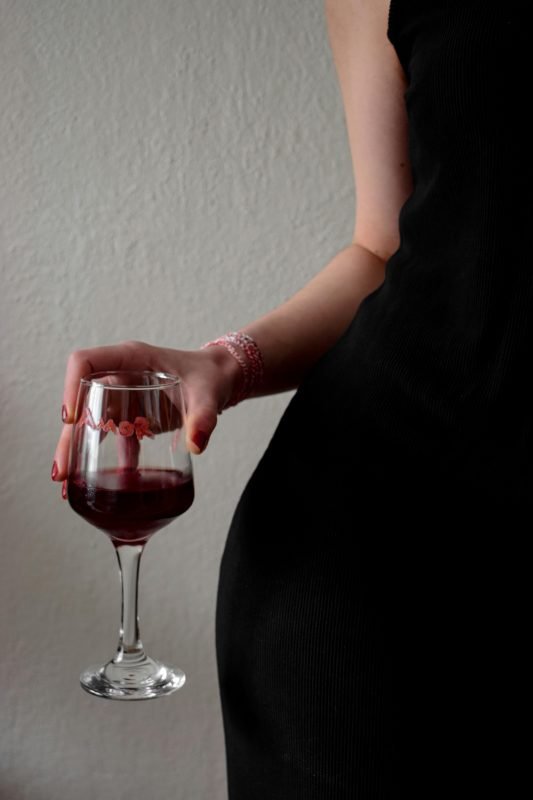 Close-up of a woman in a black dress holding a glass of red wine in a sophisticated setting.