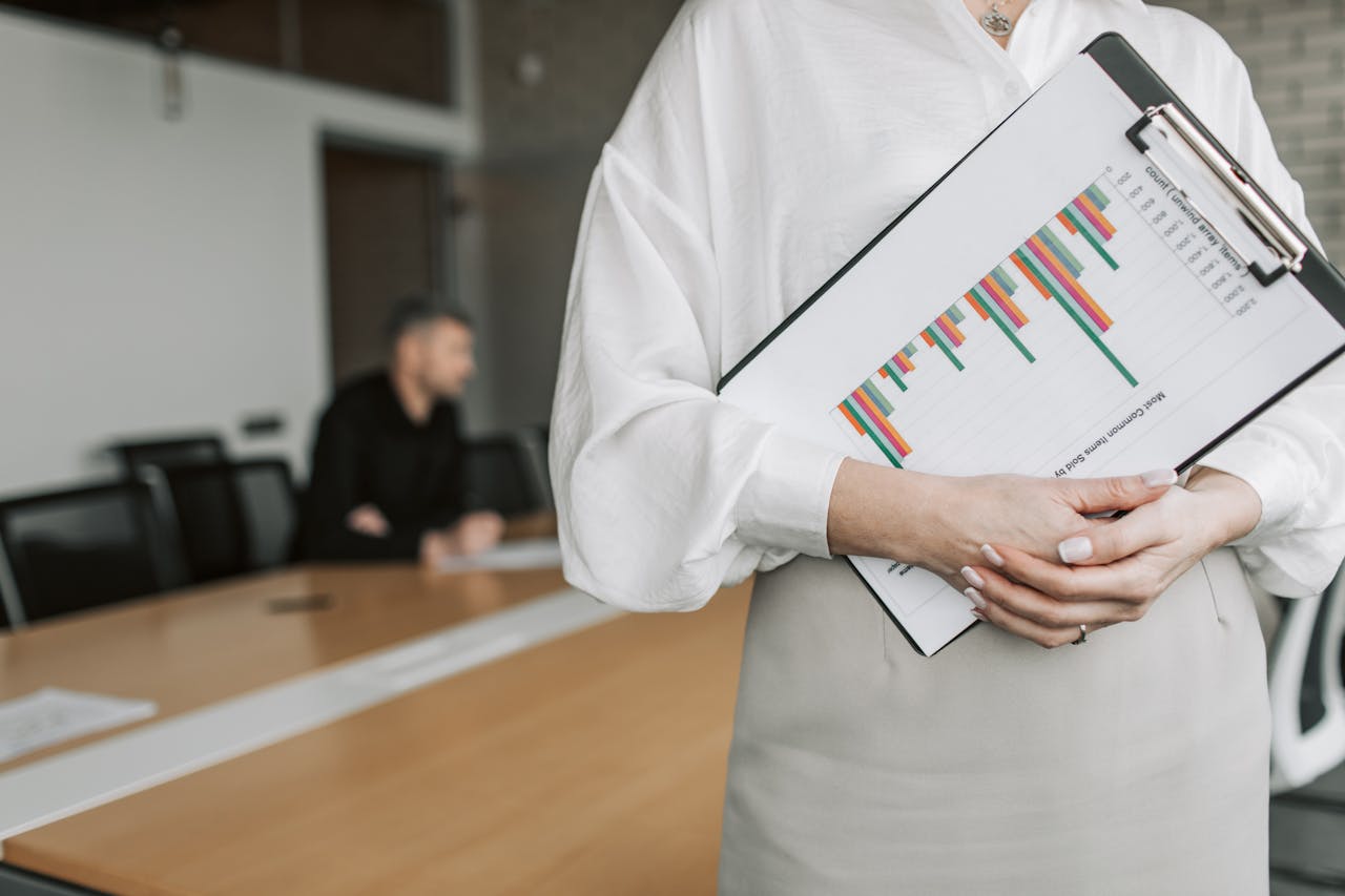 Close-up of a person holding a clipboard with charts in a meeting room.